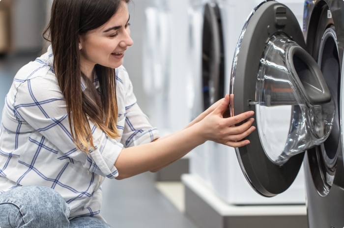Woman at a department store inspecting a floor model clothes washers in preparation for purchase.