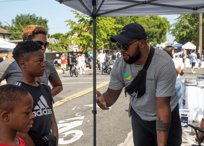 DCSEU staff person at an outdoor community event talking to two kids about energy efficiency.