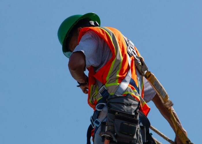 The back of a solar installer on a roof with the sky as a backdrop, adjusting their safety gear.