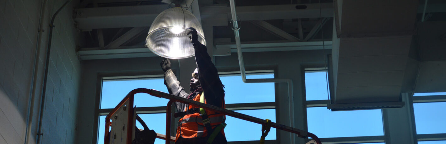 Worker on a scissor lift replacing an efficient high bay lighting fixture.