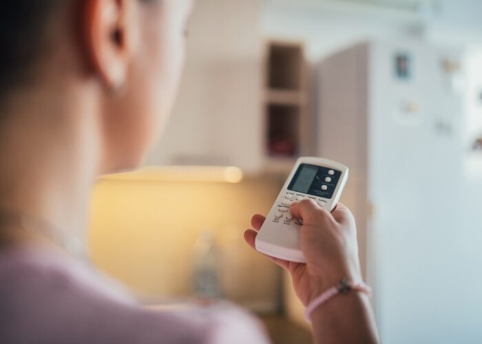 Close up of a woman using a remote to control her mini split heat pump in her kitchen.