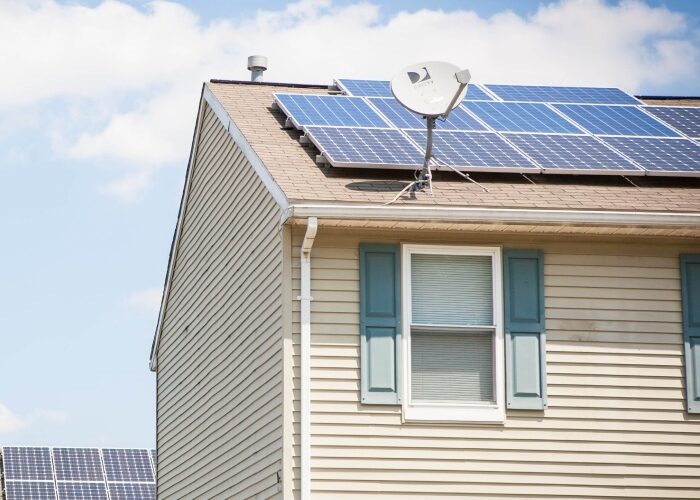 Corner of roof with solar panels and a cable dish on it with another roof with solar in the background.