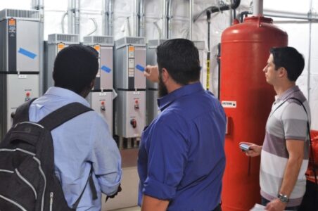 Small group of engineers inspecting a wall of variable frequency drives in a commercial building boiler room.