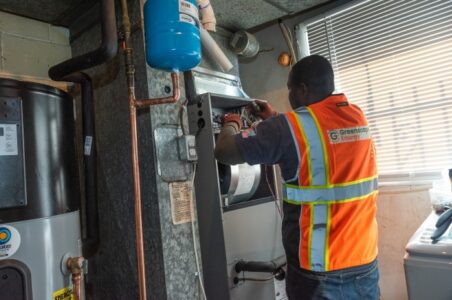 HVAC technician working on the electrical connections in an air handler of a residential heat pump in a basement.