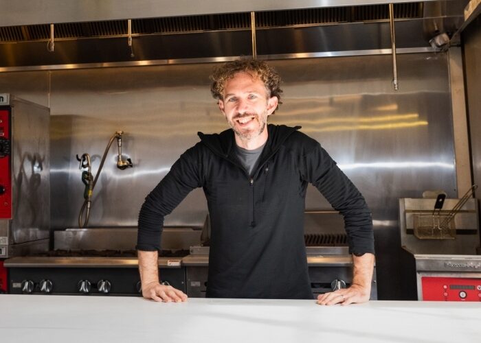 Small business owner posing in a commercial kitchen with his hands on the counter.
