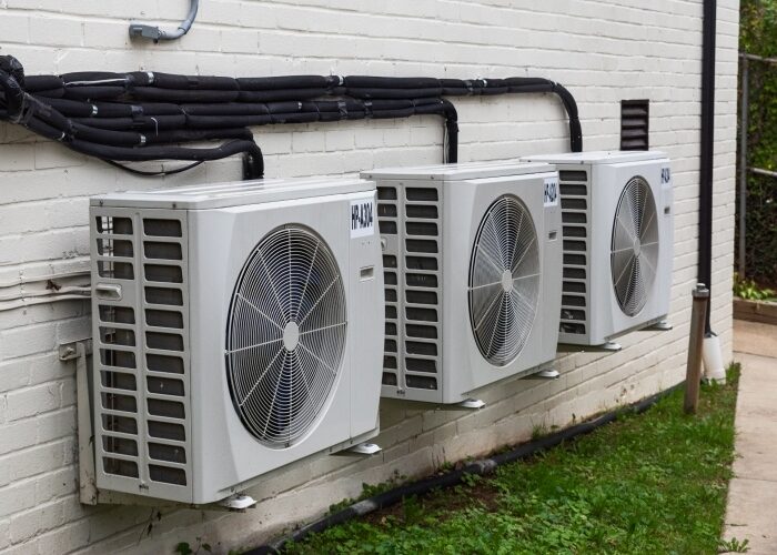 A set of three white heat pump compressors on the side of an apartment building.