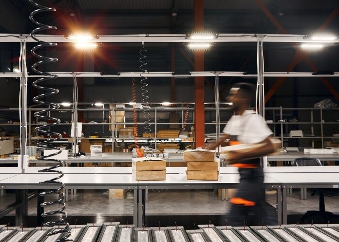 Worker in a warehouse with bright LED fixtures working at one of 3 visible production lines with packages.