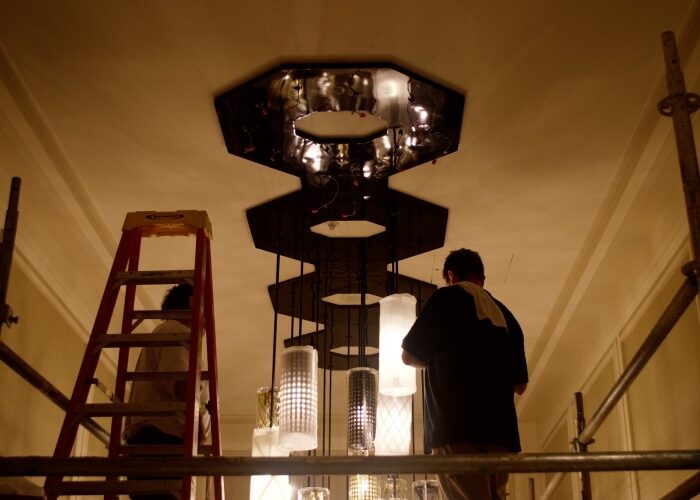 Two maintenance workers installing a large multi-pendant chandelier.