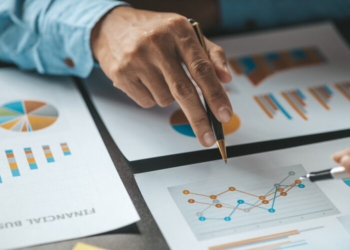 Closeup of a hand with a pen pointing to a set of financial graphs and charts.