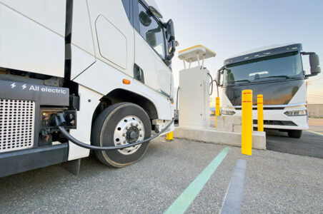 A white all-electric freight truck parked and charging at an EV charging station.