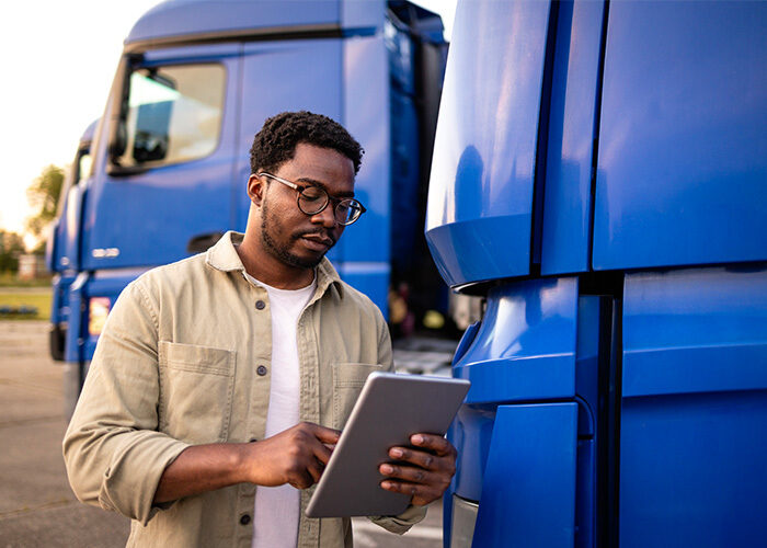 A fleet manager standing in front of a blue freight truck with a tablet reviewing information.