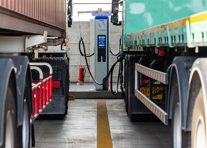 Two heavy-duty tractor trailer trucks parked and charging at the same EV charging station.