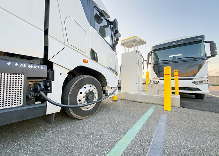 A white all-electric freight truck parked and charging at an EV charging station.