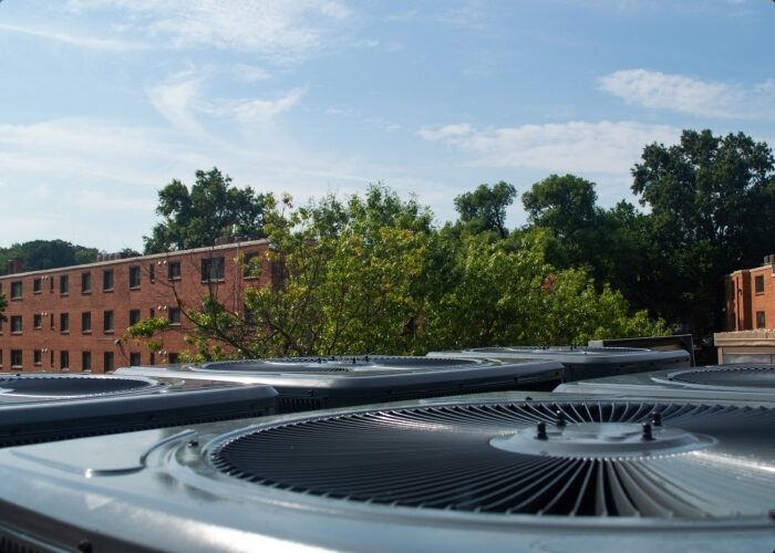 A view from atop a multifamily building maintenance roof with many air conditioner compressors in the foreground.