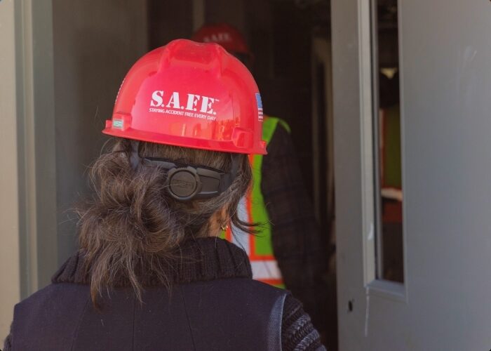 The back of a women's head with a red hardhat that reads "S.A.F.E." on it as she enters a door.
