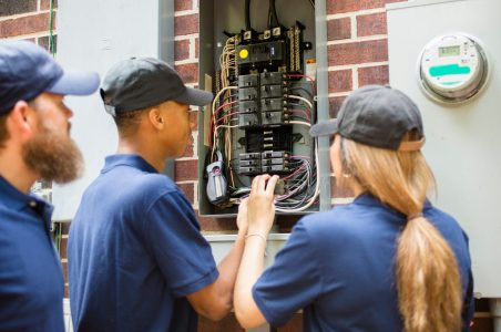 Three workers looking into a newly upgrading electric panel outside of a home.