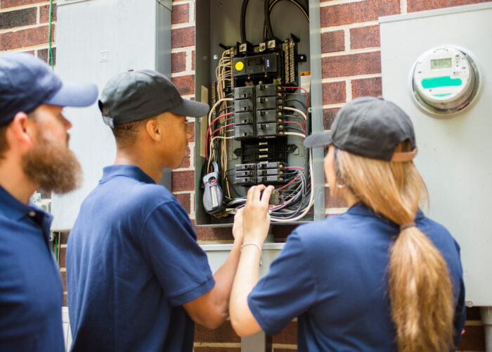 Three workers looking into a newly upgrading electric panel outside of a home.