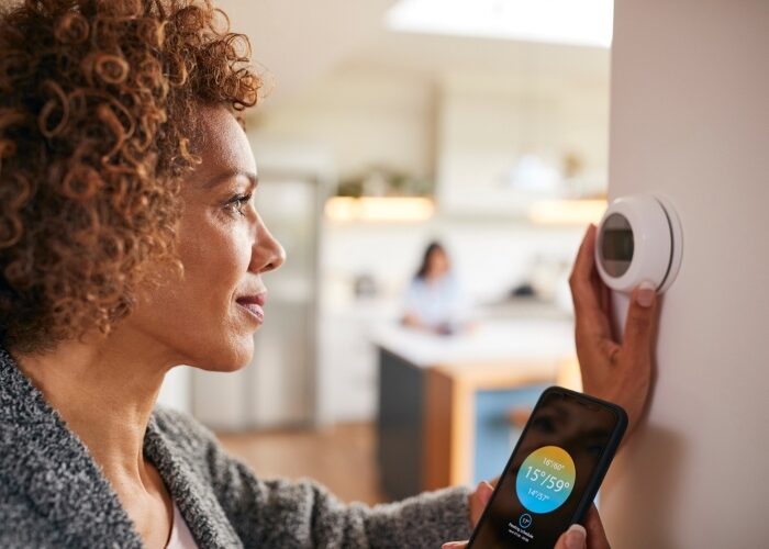 A woman near the kitchen adjusting her smart thermostat and checking her phone.