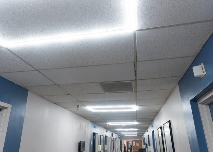 Ceiling view of LED halo light fixtures going down the hallway of an institutional building.