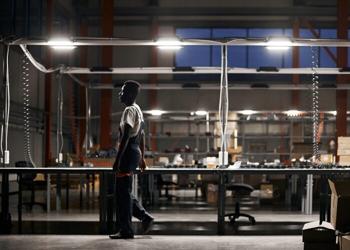Worker in a warehouse with bright LED fixtures working at one of 3 visible production lines with packages.