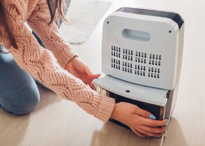 A women kneeling on the floor of her home replacing the water tank on a small dehumidifier.