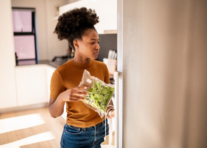 Women opening her refrigerator to place a bag of food in it.