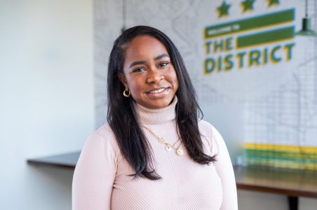 Graduating extern and DCSEU Social Media and Events Coordinator, Karlene, smiling in an office setting with a pink turtleneck on.