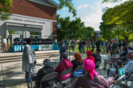 DCSEU managing director providing remarks in front of the Parkside community center steps to residents with tables filled with energy kits for distribution in the background.