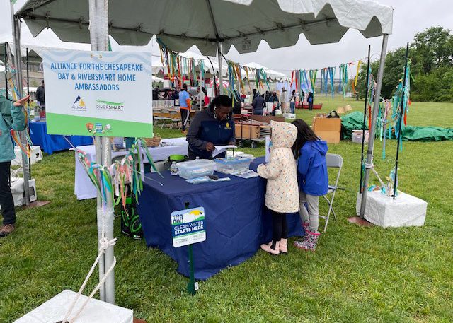 DCSEU staff, Yvonne Coles, tabling at the Anacostia River Festival sharing information about DOEE's RiverSmart program with two children.