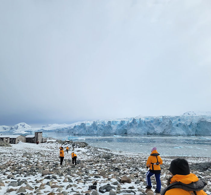Overcast arctic landscape of Stonington Island with the ocean in the mid-ground and five explorers traversing the foreground.