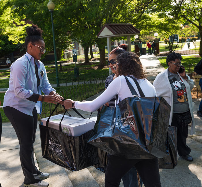 DCSEU staff members passing a energy kit bag to two Parkside residents in an open courtyard.