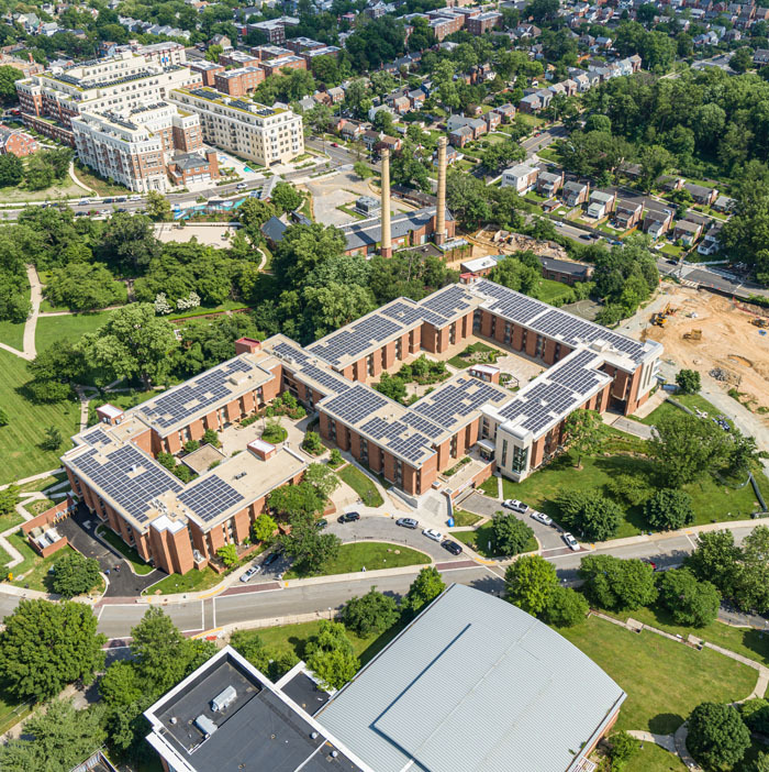 Aerial cityscape of Abrams Hall Senior Apartments that hold a large community solar array on its roof with surrounds roads and foliage.