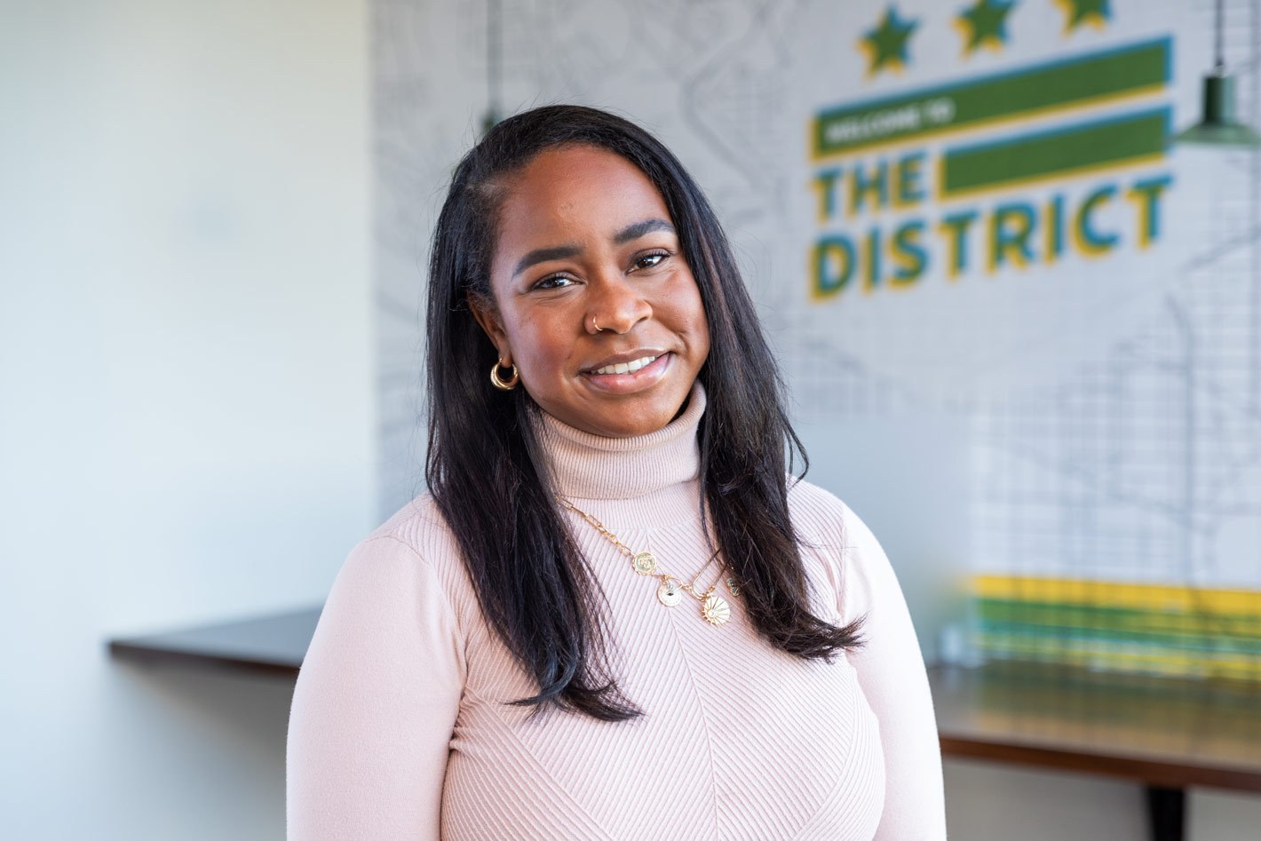 Graduating extern and DCSEU Social Media and Events Coordinator, Karlene, smiling in an office setting with a pink turtleneck on.