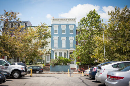 A light blue dc row home on a sunny day taken from across the street in a parking lot.