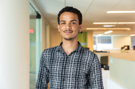 Aldric, a young man in the DCSEU workforce development program, posing for a portrait in an office setting wearing a black and gray plaid button down shirt.