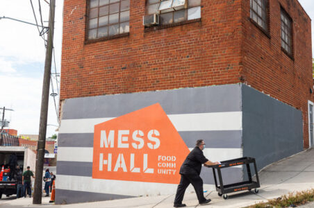 Culinary worker pushing a cart in front of the Mess Hall building mural.