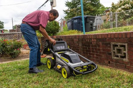 Mr. Woodfin, an African American District resident, changing the clippings bag on his electric lawn mower in his backyard.