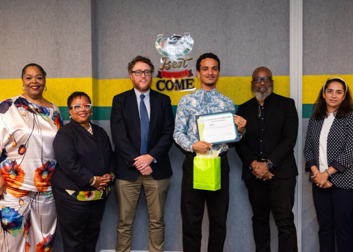 Aldric posing for a photo with DCSEU staff, advisory board members, and the keynote speaker at the workforce development program graduation. He is holding his graduation certificate and all six people pictured are smiling.