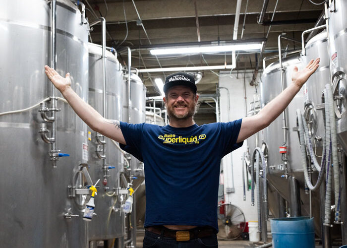 DC Brau Co-Founder and Brewmaster Jeff Hancock smiling and holding his hands out in front of two rows of fermenter tanks.