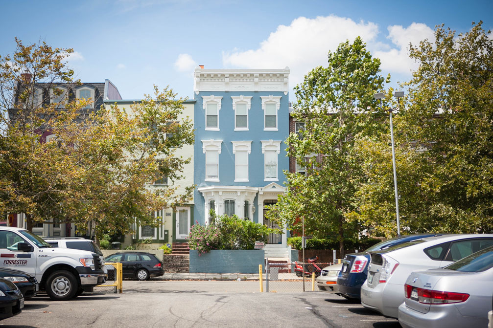 A light blue dc row home on a sunny day taken from across the street in a parking lot.