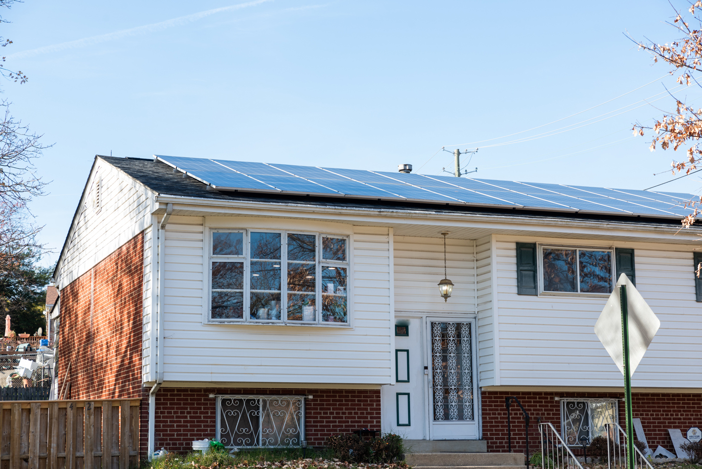 A white and brick colored split level single-family home in Ward 7 with solar panels on the roof on a sunny day with a blue sky above it.