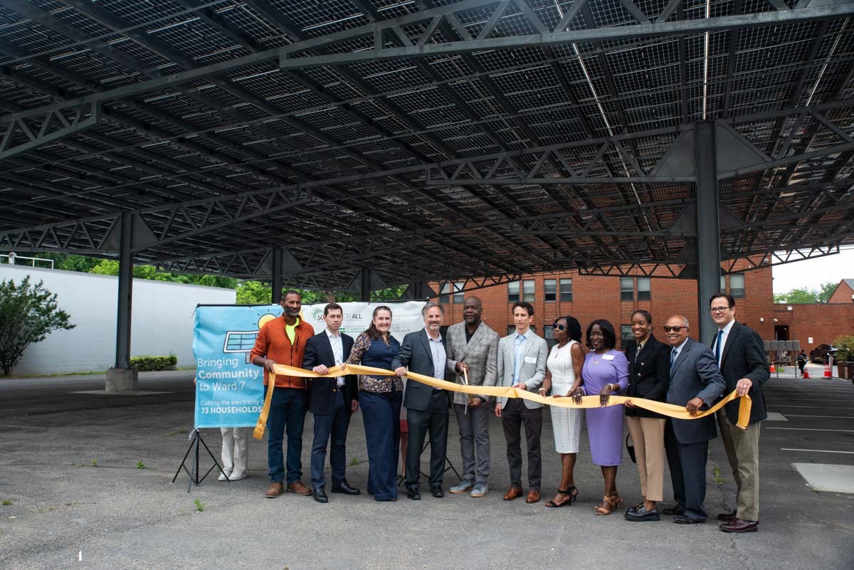 Group of principals under Sargent Memorial's parking lot community solar canopy cutting the grand opening ribbon.