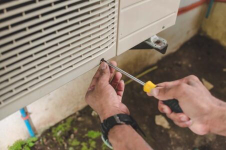 Closeup of a person using a screwdriver on a heat pump compressor.
