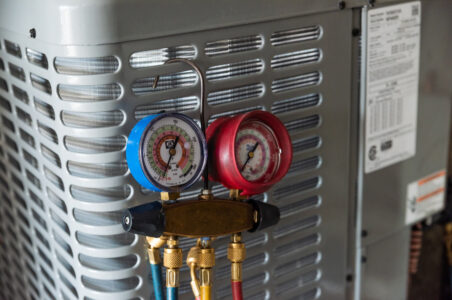Closeup of yellow jacket manifold gauges with four valves and hoses hanging on a newly commissioned heat pump compressor.