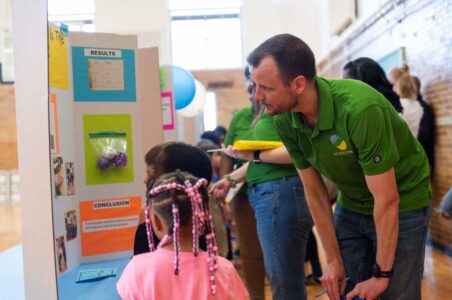 DCSEU staff squatting down listening to Pre-K aged students from Langley Elementary School presenting their STEM fair project.