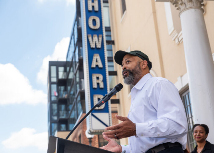 DOEE Director Richard Jackson providing remarks at a podium in front of the Howard Theatre with the marquee sign in the background.
