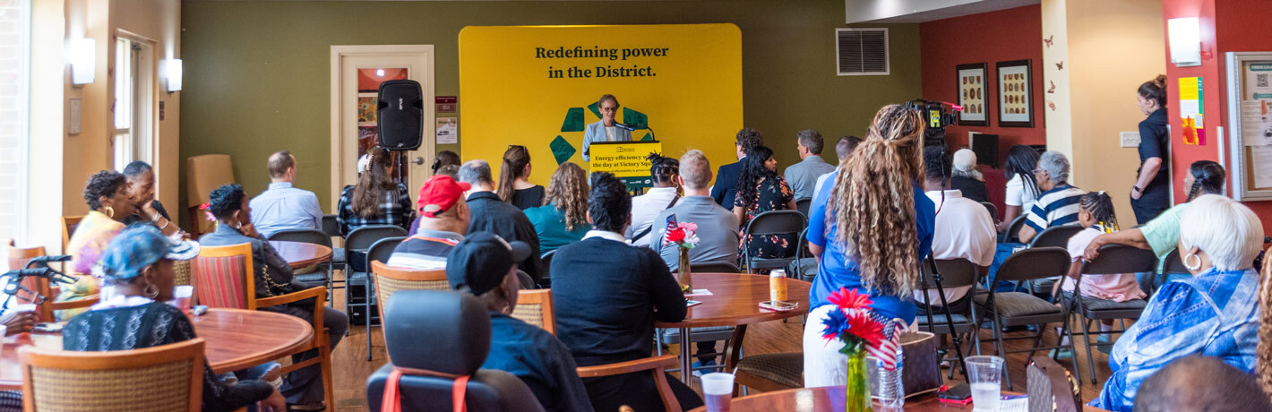 Full community room of project partners and building residents watching remarks from Victory Housing's CEO.