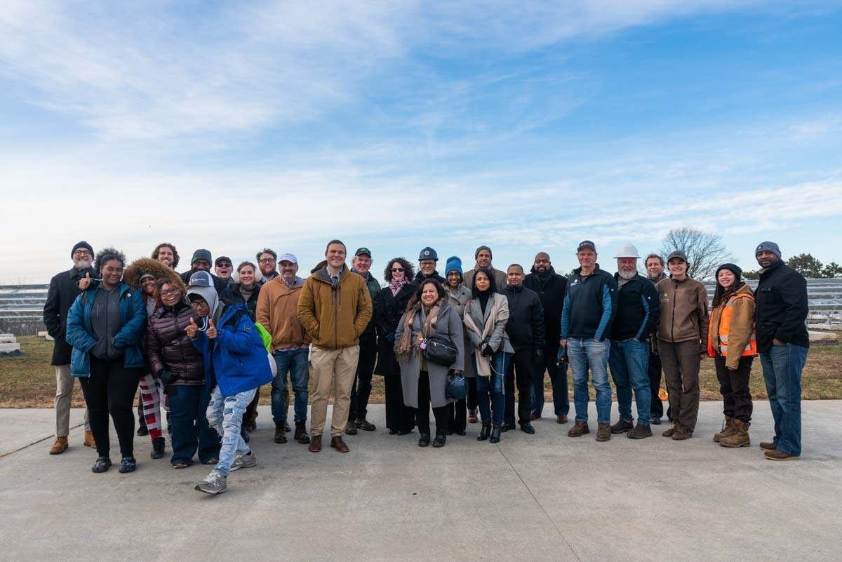 Large group of students, government officials, and project staff posing in front of Brentwood Reservoir community solar site under construction.