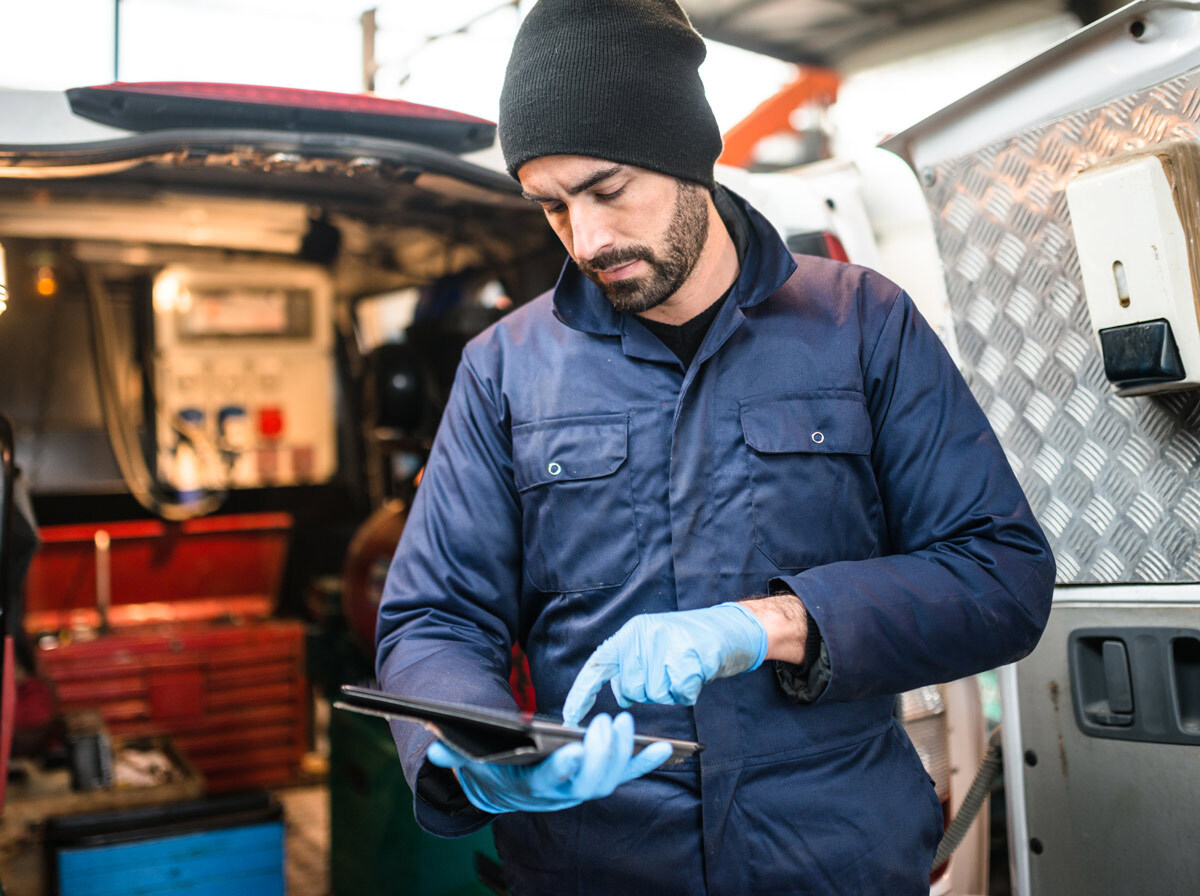 A contractor holding a tablet behind his work van.