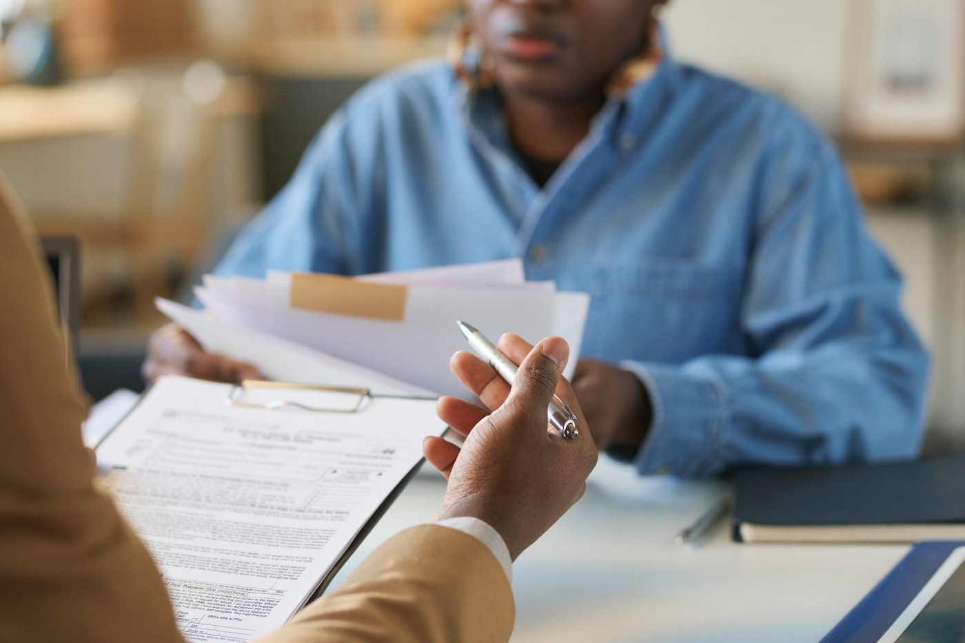 Close up of the hands of a tax accountant reviewing tax returns with a client sitting across from them. The accountant is pointing to parts of the document while the client is holding additional forms and listening intently.